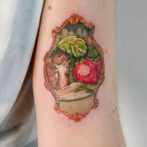 Unique upper arm tattoo featuring a rat, strawberry, and frame design by Juliany Braga.