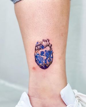 A beautiful illustrative tattoo of a flower and heart on the lower leg, designed by the talented artist Juliany Braga.
