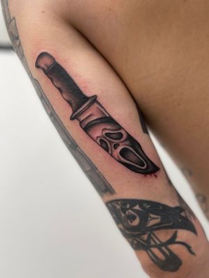 An illustrative blackwork tattoo of a knife, mask, and scream, beautifully crafted by Miss Vampira on the upper arm.
