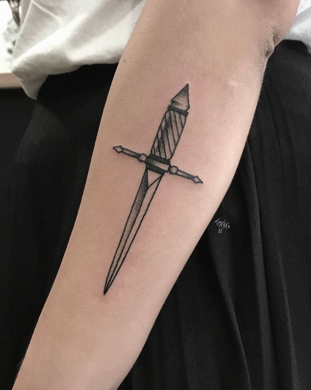 Fine line rose and dagger tattoo on the forearm.
