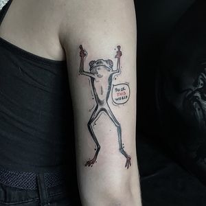 Emiliia Kuzmina's illustrative frog tattoo on upper arm features a meaningful quote in stylish lettering.