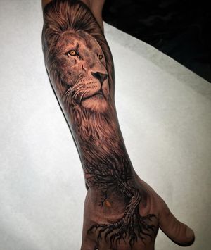 Immerse yourself in the majestic beauty of this black and gray tattoo featuring a lifelike lion and intricate tree by artist Justin JP Param.