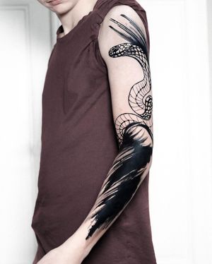Blackwork illustrative tattoo by Joza featuring a striking snake and intricate pattern design on the lower arm.