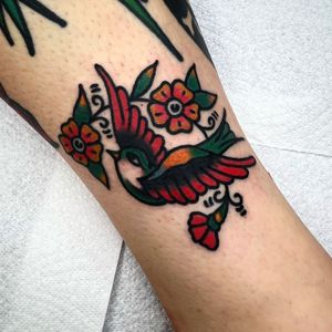 A vibrant traditional tattoo on the arm featuring a beautiful bird and flower motif, skillfully crafted by Alessandro Lanzafame.