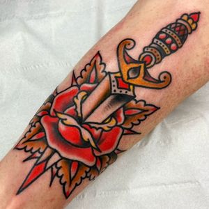 A stunning traditional tattoo featuring a vibrant flower and sharp dagger, expertly executed by tattoo artist Alessandro Lanzafame on the forearm.