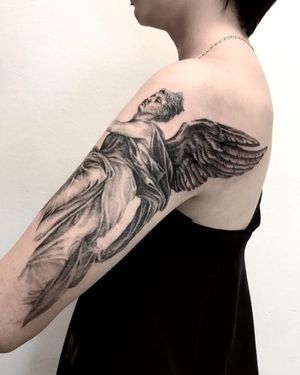Get inked with a mesmerizing blackwork angel statue tattoo on your upper arm by talented artist Juli Liverinova.