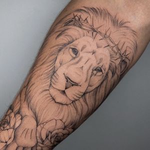 Get a bold and intricate tattoo masterpiece by Irene Bogachuk, featuring a majestic lion and delicate flower design on your forearm.