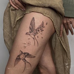 Fine line and illustrative blackwork tattoo featuring a bird and flower motif on the upper leg by Irene Bogachuk.