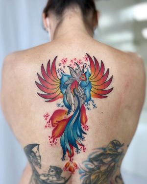 Mesmerizing illustrative phoenix tattoo on back by artist Vic. Vibrant watercolor shades bring this mythical bird to life.