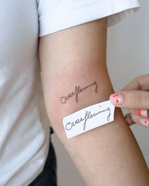 Elegant fine line script tattoo on upper arm. Perfect for a subtle and meaningful piece of art.