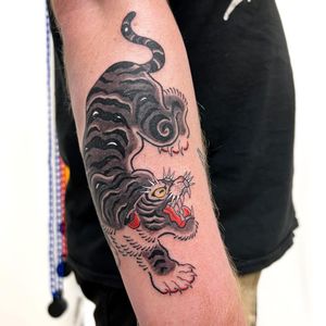 Experience the power and grace of a majestic tiger in this bold and vibrant illustrative forearm tattoo by Leo Quintao.