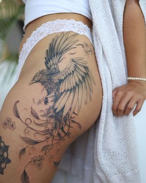 Experience the beauty of a blackwork and illustrative tattoo by Sasha Sunshine, featuring a stunning fusion of a flower and phoenix motif on the upper leg.