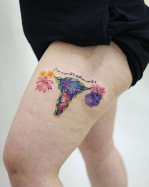 Empower yourself with this stunning watercolor galaxy tattoo featuring a floral design and a powerful feminist quote by artist Cerf on your upper leg.