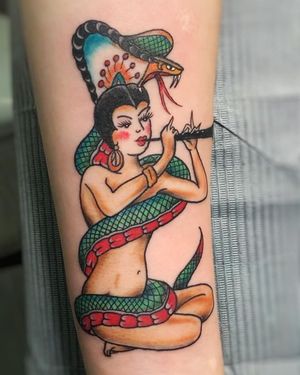Traditional forearm tattoo featuring a woman playing a flute with a snake intertwining around her, by artist Steven Brooks.
