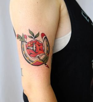 Get a stunning traditional tattoo on your upper arm featuring a beautiful flower and lucky horseshoe by artist Liza Vettaa.