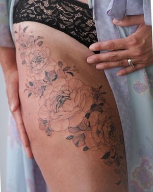Beautiful upper leg tattoo featuring a delicate flower design by Sasha Sunshine. The fine line work and ornamental style make this piece a stunning addition to your body art collection.