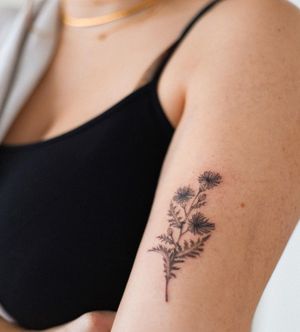 Elegant blackwork flower design by Yasmin Clara for a stunning upper arm tattoo.