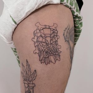 Illustrative upper leg tattoo by Nicole Ksiazek featuring aku aku mask and bones in a bold blackwork style.