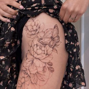 Illustrative upper leg tattoo featuring a butterfly and flower, by Irene Bogachuk. Beautiful and bold black ink design.