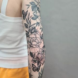 Experience the beauty of nature with this stunning blackwork tattoo by Liza Vettaa. A delicate butterfly and flower design perfect for your sleeve.