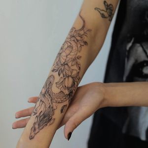 Experience the juxtaposition of strength and beauty with this blackwork dragon and flower forearm tattoo by Palena.