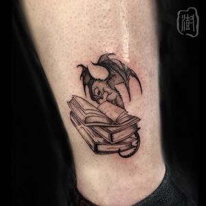 Express your love for fantasy with this striking blackwork dragon and book tattoo on your ankle by artist Cerf.