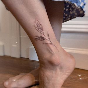 Beautiful illustrative ankle tattoo featuring a delicate flower and leaf design by Irene Bogachuk.