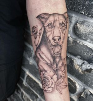Unique forearm tattoo featuring a dog, flower, collar, and name in striking blackwork style by Palena.