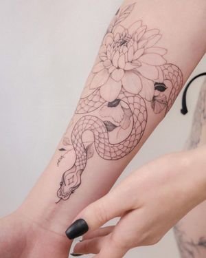 Elegant forearm tattoo by Sasha Sunshine featuring a delicate snake entwined with a blooming flower in fine line style.