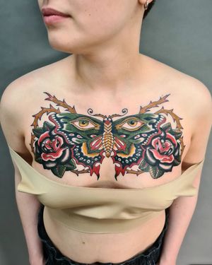 Beautiful traditional chest tattoo by Liza Vettaa featuring a striking design of a moth, flower, eye, and thorns.