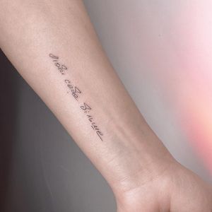 Elegantly inked fine line and small lettering tattoo on forearm featuring a meaningful quote by renowned artist Irene Bogachuk.