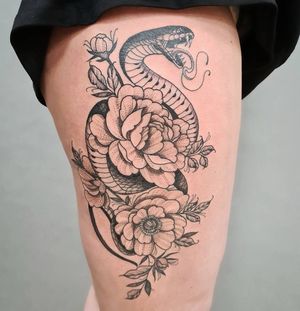 Illustrative upper leg tattoo by Liza Vettaa featuring a striking snake intertwined with a beautiful flower design.