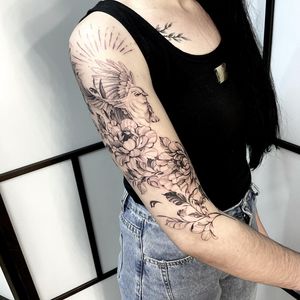 Elegant upper arm tattoo by Nicole Histon featuring a beautiful blackwork bird and flower design. Perfect for those who appreciate illustrative style tattoos.