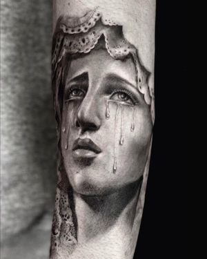 Intricate black and gray tattoo on forearm featuring a woman shedding tears, reminiscent of the Virgin Mary. By Mengni Yang.