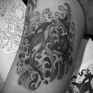 Get a stunning black and gray illustrative tattoo of a whale and dolphin by Tom Cobra on your upper arm.