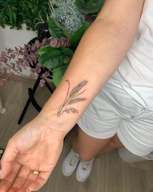 Elegant forearm tattoo by Alina Ivenko featuring a delicate flower sprig design in fine line style.