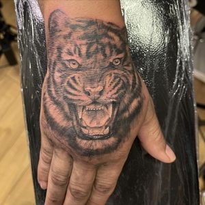 Get fierce with this stunning black and gray tiger tattoo on your hand. Pablo's illustrative style brings this majestic animal to life.