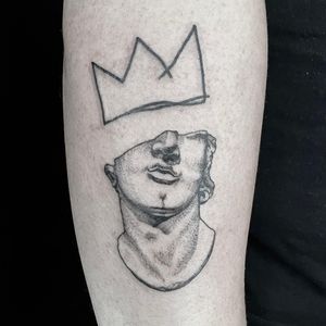 Elegant blackwork tattoo on upper arm by Brian Daka featuring a crown and statue motif. A truly royal piece of art.
