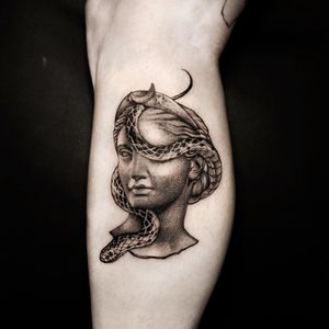 Unique lower leg tattoo featuring a snake, statue, and woman designed by Oek. Bold blackwork style with intricate details.