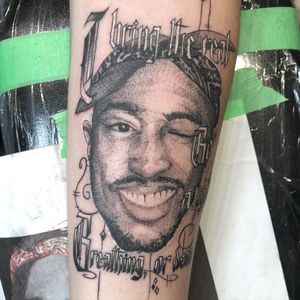 Embrace the iconic words of Tupac with this black and gray forearm tattoo featuring realistic lettering and illustrative elements by Pablo.