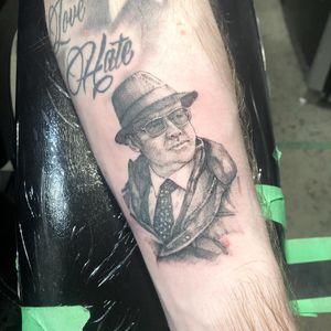 Stunning black and gray forearm tattoo featuring a man with a hat and glasses, done by the talented artist Pablo.
