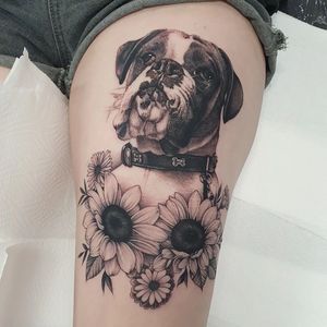 Dani Mawby's blackwork tattoo features a detailed dog wearing a collar, surrounded by a beautiful sunflower illustration on the upper leg.