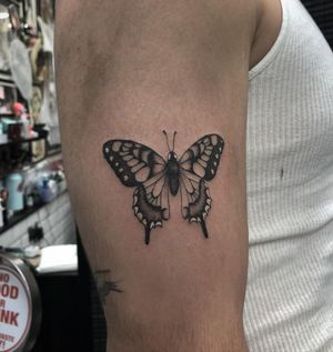 Get a stunning black and gray butterfly tattoo on your upper arm in London, GB. Embrace elegance and beauty with this timeless design.
