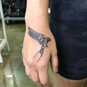 Adorn your hand with this exquisite black and gray fine line illustrative tattoo featuring a beautiful bird and delicate filigree details, crafted by the talented artist Carlos Hernandez.