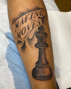 A striking blackwork forearm tattoo by Carlos Hernandez featuring a regal quote and chess motifs.