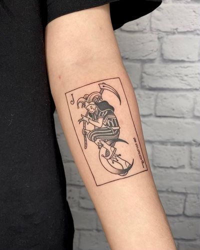 Unique blackwork & fine line design by Marcos featuring moon, joker, card, scythe & man motifs on forearm.