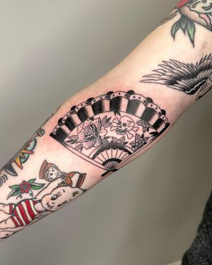 Illustrative forearm tattoo by Sasha featuring a unique combination of floral, skeletal, and fan motifs.