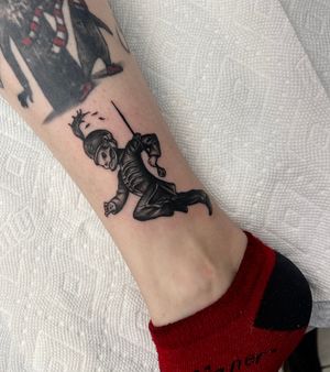 Blackwork lower leg tattoo featuring sword, helmet, and soldier motifs, by Miss Vampira. Illustrative style.