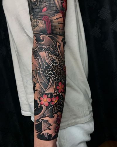A stunning sleeve tattoo by Avi featuring traditional Japanese motifs of koi fish, cherry blossoms, and crashing waves.