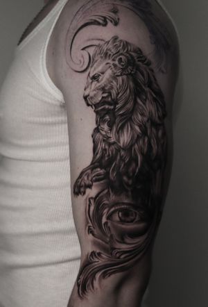 Impressive upper arm tattoo in black and gray by Alejandro Gonzalez, featuring a detailed lion eye adorned with intricate filigree design.